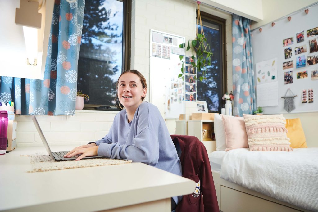 A happy girl is seated at a desk in her dorm room at AƬ's Anglican Girls School.