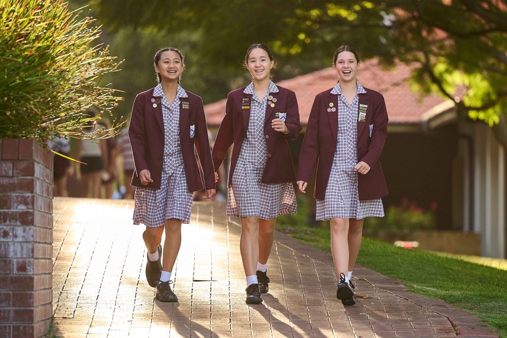 Three girls in school uniforms walking down a brick path at AƬ's Anglican Girls School.
